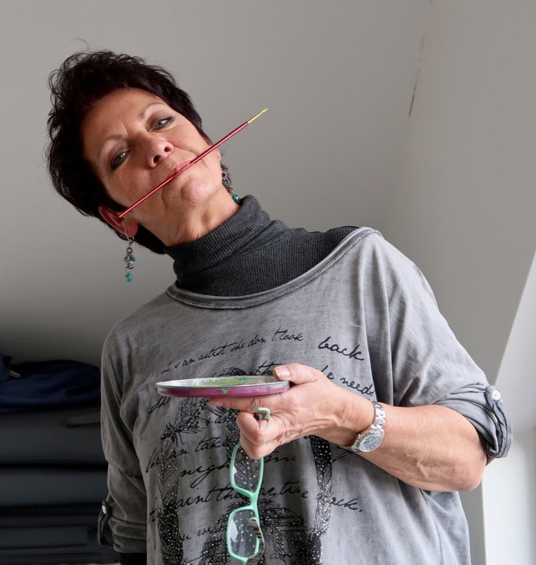 Künstlerin Heidemarie Brosien mit Pinsel im Mund und einer Farbschale in der Hand
